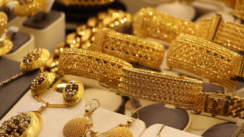 Stack of gold bars and vintage pocket watch on dark fabric